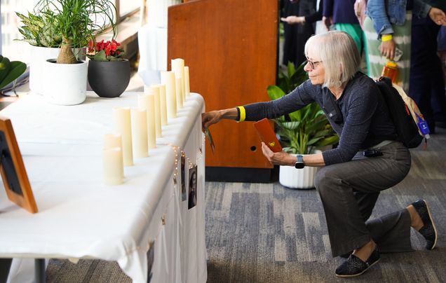 Woman kneeling before a table covered in a white tablecloth with many tall white pillar candles