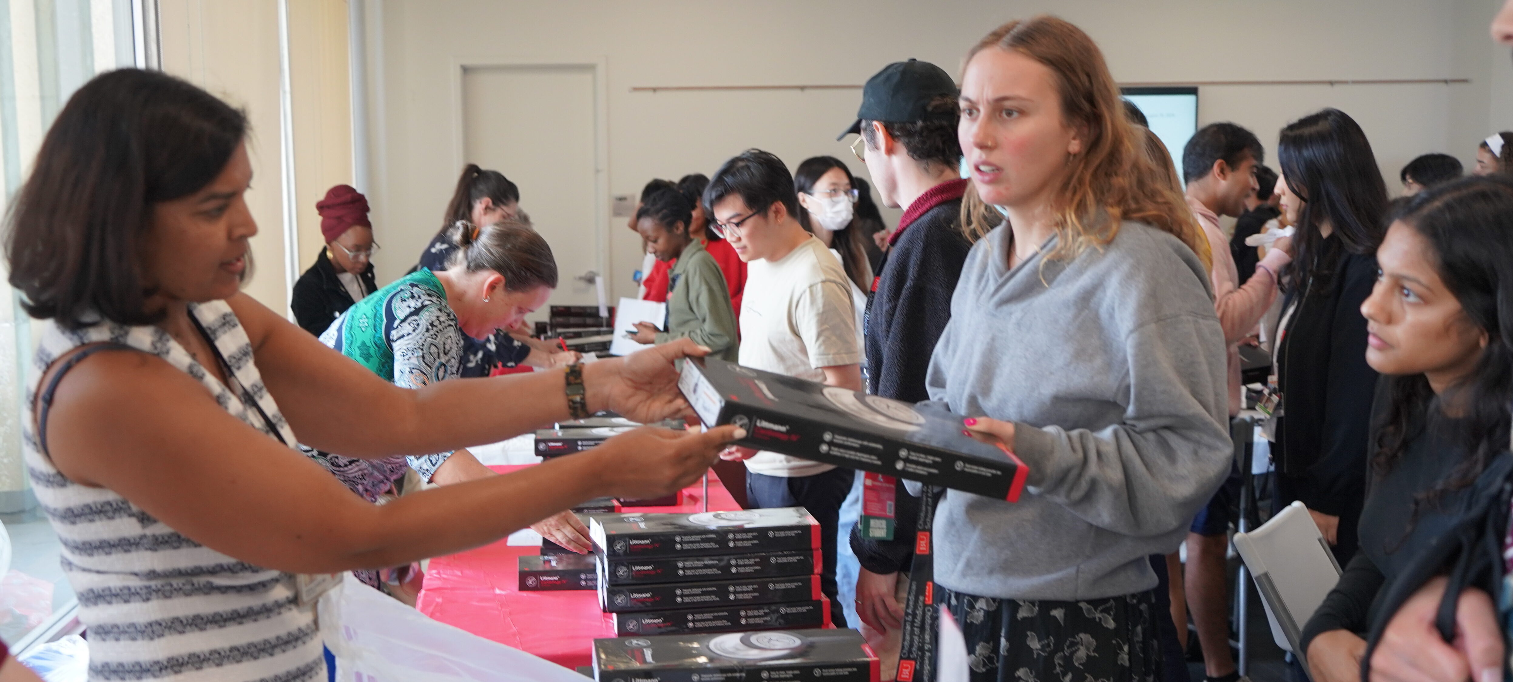 Standing behind a long white table Priya Garg, MD hands students medical instrument packages