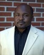 Head and shoulders of Eric Brown in white suitcoat infront of brick wall