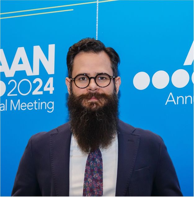 Head and shoulders of Dr. Charidimou wearing a suit and tie in front of blue banner