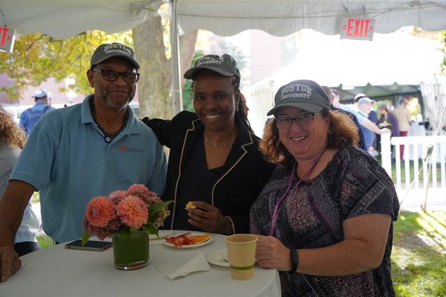 Three people wearing new BU Inauguration hats and smiling at a table with small plates
