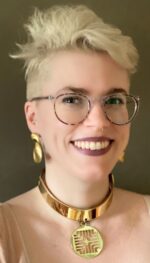 Woman with short blond hair, eyeglasses, gold earrings and necklace smiling broadly