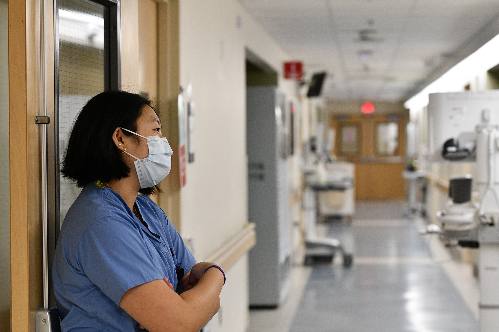 Woman medical student in blue scrubs leaning against hall wall in hospital