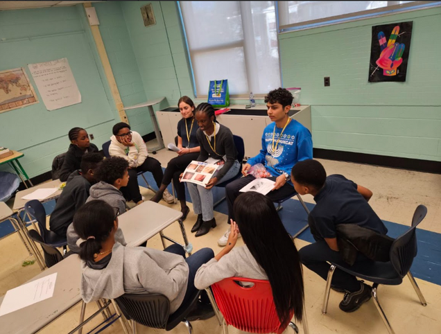 A group of students sits in a circle in a classroom, engaged in a discussion.