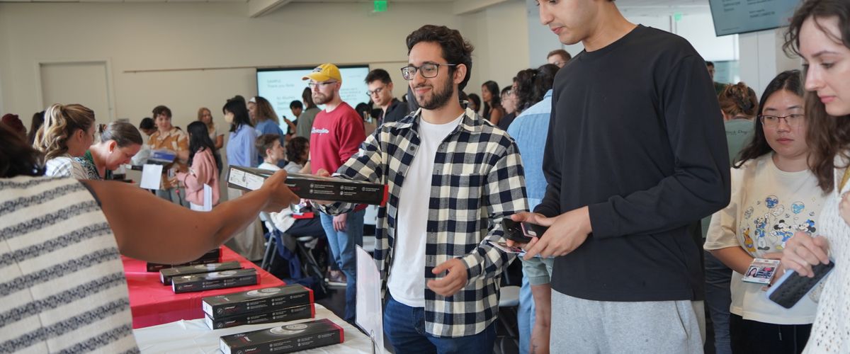 People standing in line at a distribution table receiving items in a crowded room.
