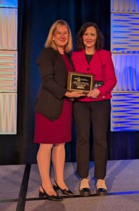 Denise Sloan in red jacket and black pants receiving Lauffer award from woman in burgandy dress and black jacket