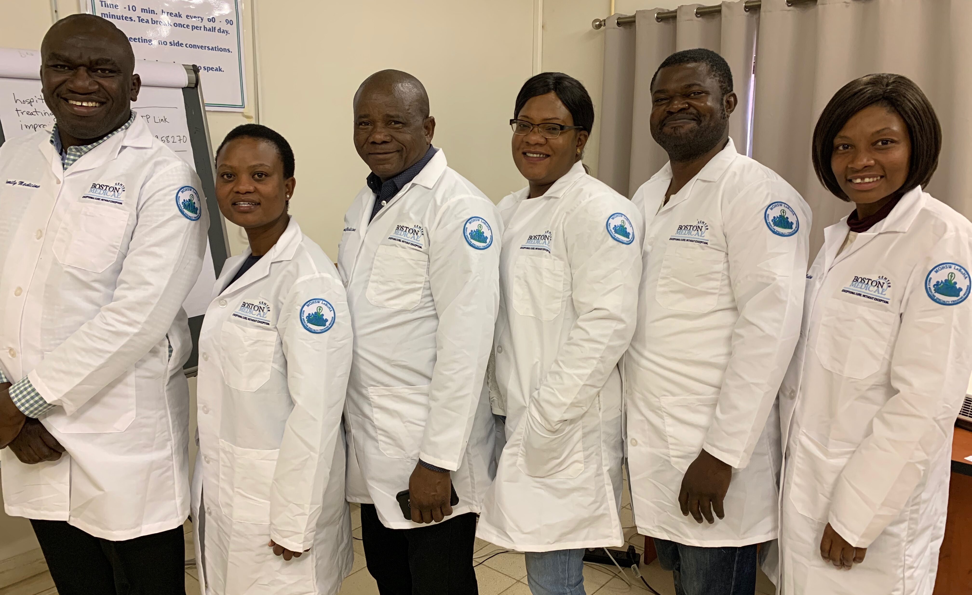 Six residents wearing white coats smiling broadly