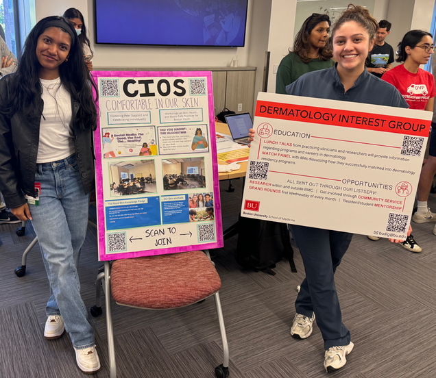 Two students representing the Comfortable in Our Skin advocacy group and Dermatology Interest Group, respectively, at a fair.
