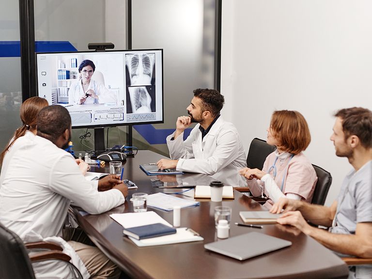 Five men and women gathered around conference table viewing large video screen.