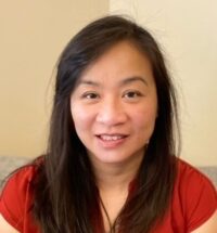head and shoulders shot of Cindy Yee-Lin long dark hari parted on the side, wearing red top, smiling