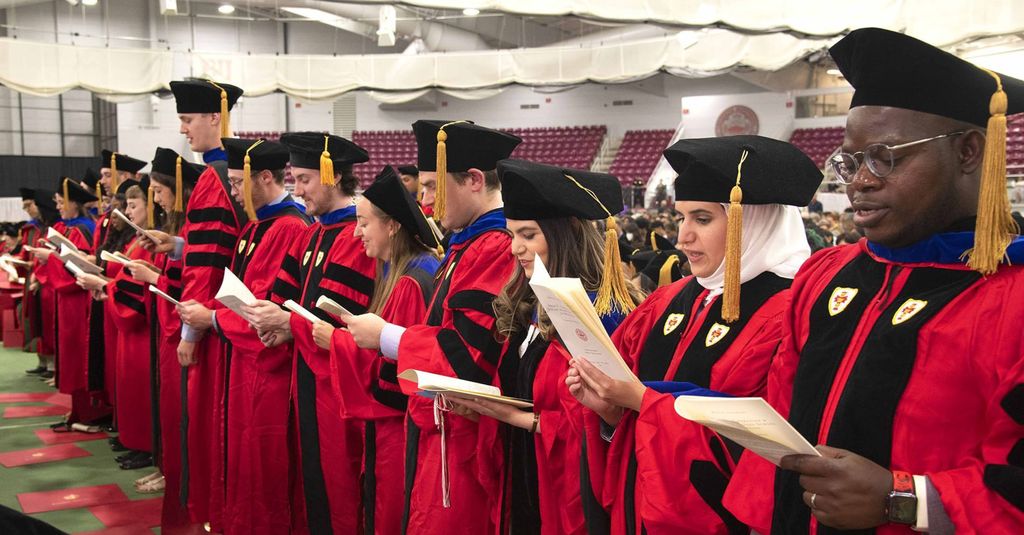 PhD graduates standing reading Oath of the Scientist after being hooded.