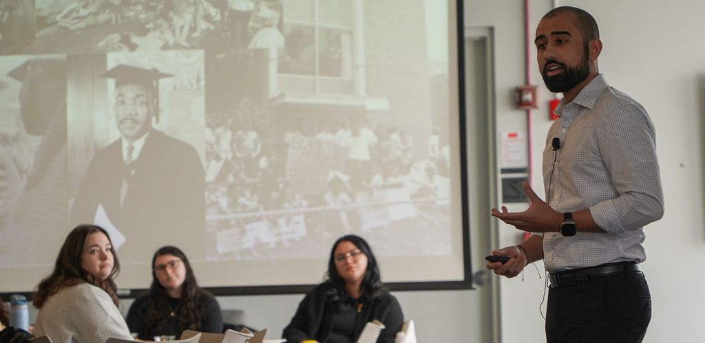 Neil Bedi standing and talking infront of people seated, MLK pictures in background