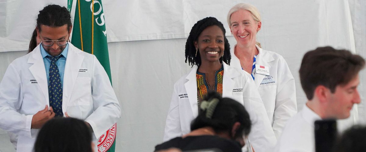 Three individuals wearing white lab coats during a ceremony or formal event