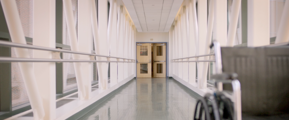Corridor with large windows, white walls, handrails, and wheelchair access in a medical facility.