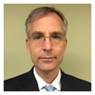 head and shoulders of Kay Leissner wearing white shirt and dark suitjacket. He has gray hair and wears rimless eyeglasses