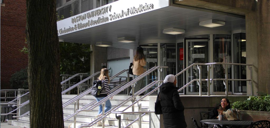 Entrance to Boston University's Chobanian & Avedisian School of Medicine, with stairs, handrails, and several people near the doorway and seated outside.