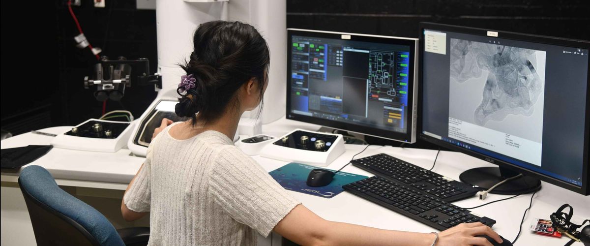 A person analyzing medical imaging on multiple computer monitors in a lab setting, with advanced equipment visible on the desk.