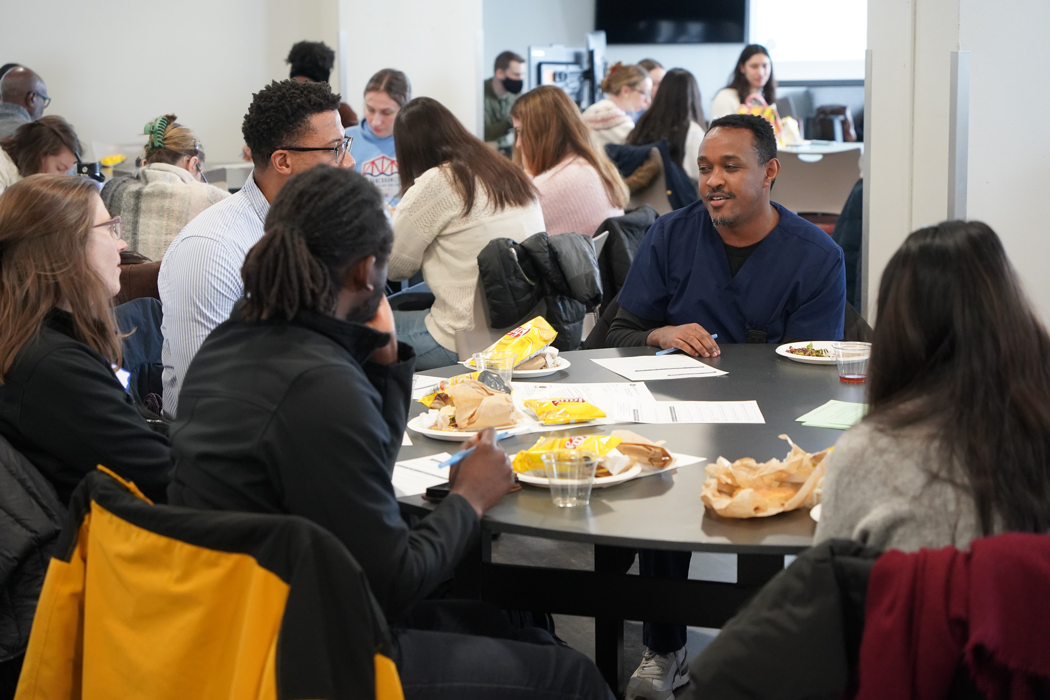 Students, faculty and staff seated at tables talking and eating lunch