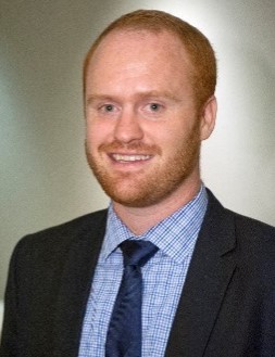 Red headed man with short-cropped hair, wearing a suit and smiling