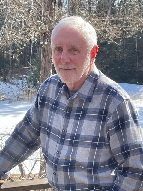 Mort Salomon, a man whose lived many years, stands with sunshine lighting from behind along a porch outside his Massachusetts home.