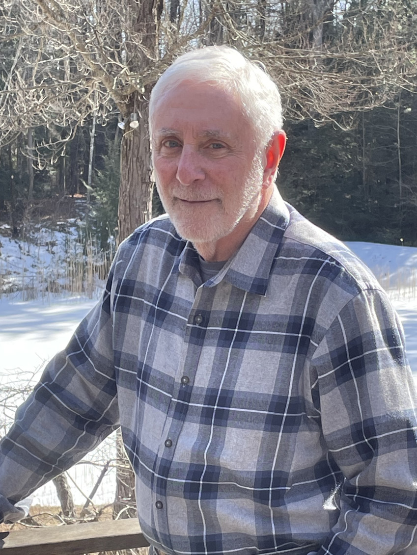 Mort Salomon, a man whose lived many years, stands with sunshine lighting from behind along a porch outside his Massachusetts home.