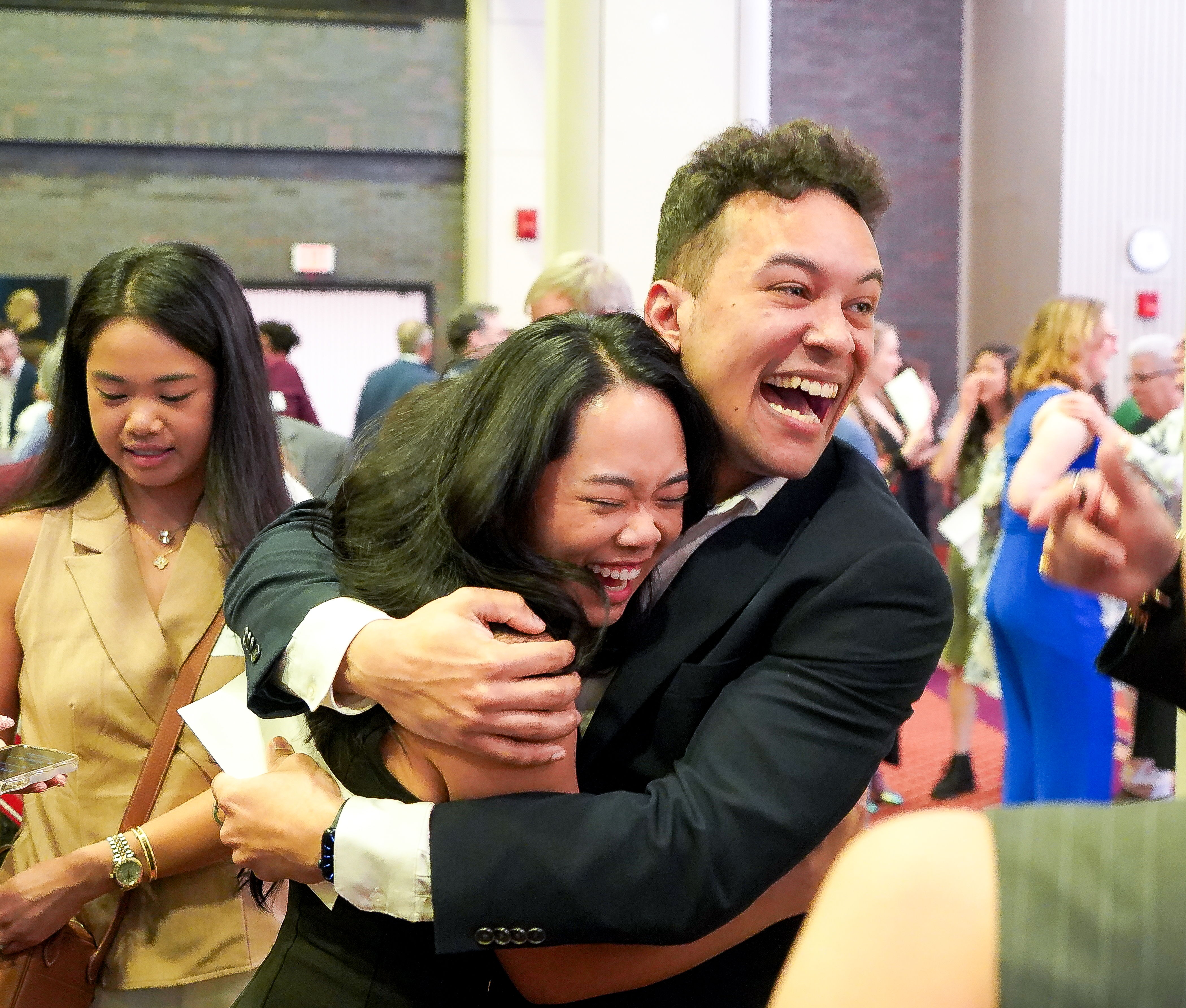 Man and woman embracing, wide smiles holding white papers with Match Day results
