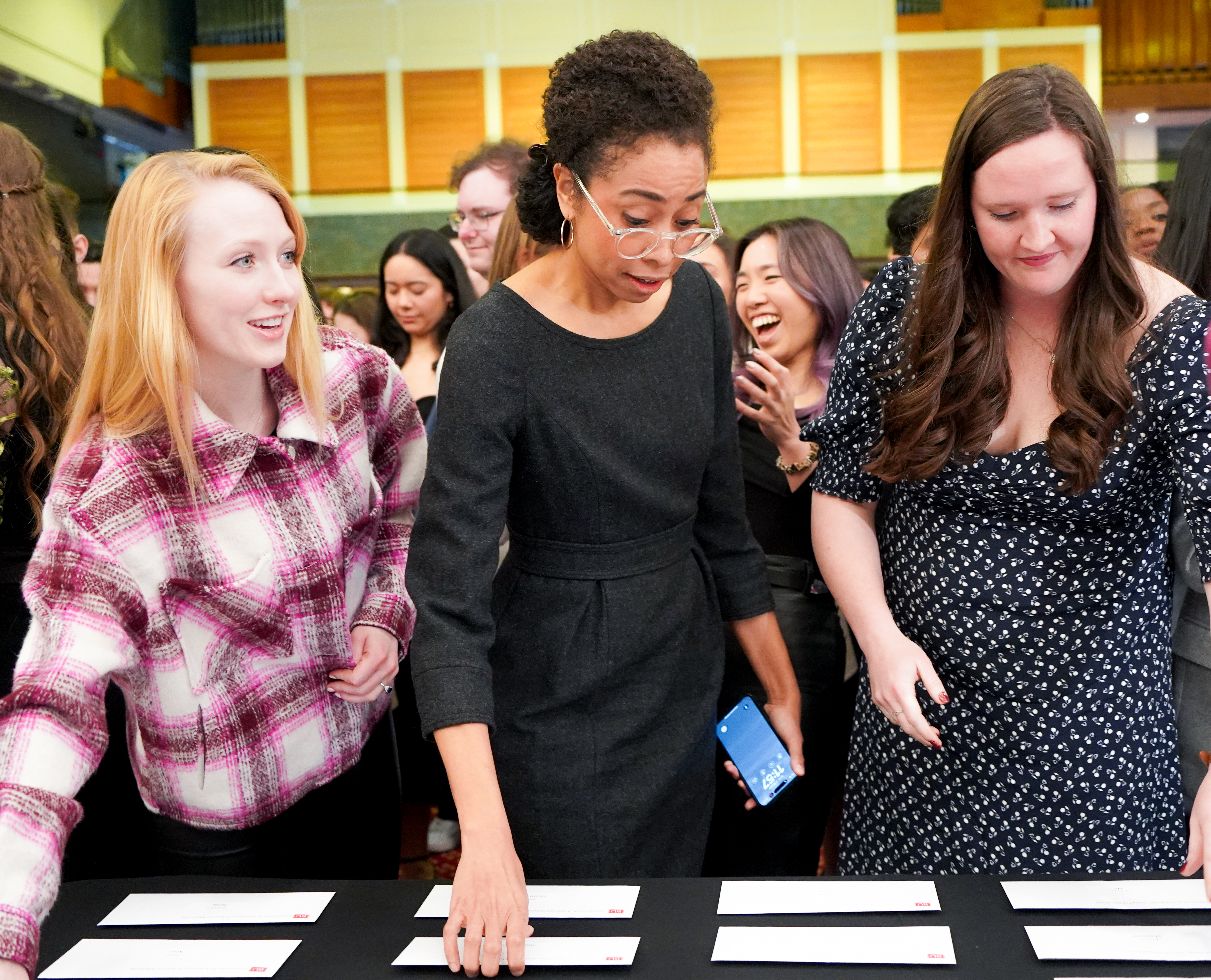 Three women staging in front of a table reaching for envelopes that hold Match Day residency results