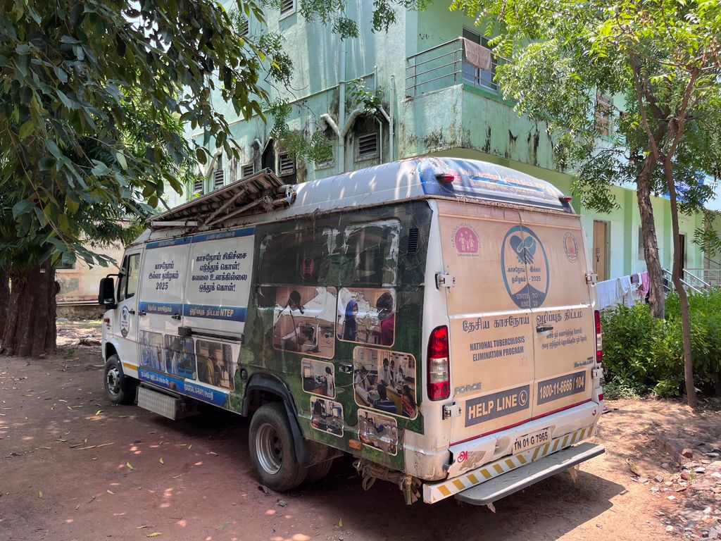 Small van with lots of signage on city street surrounded by trees and tall buildings