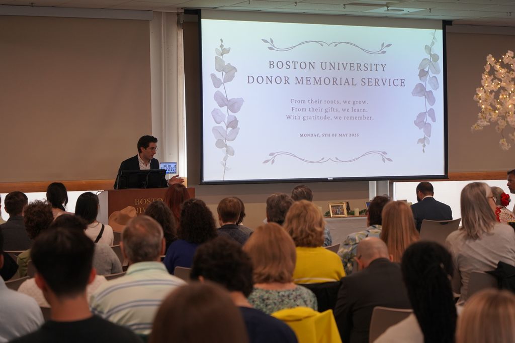 Student stands at podium in front of screen welcoming people to the ceremony