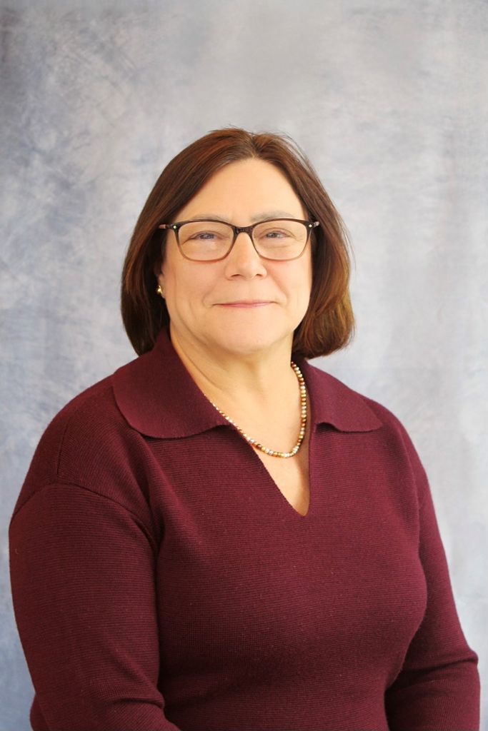 Laura Anastasi burgandy top, chin length brown hair, eye glasses, gentle smile