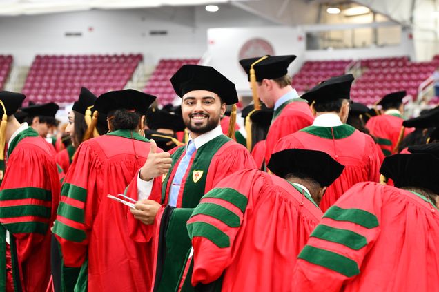 students in regalia walking to their seats, one looks back and gives thumbs up