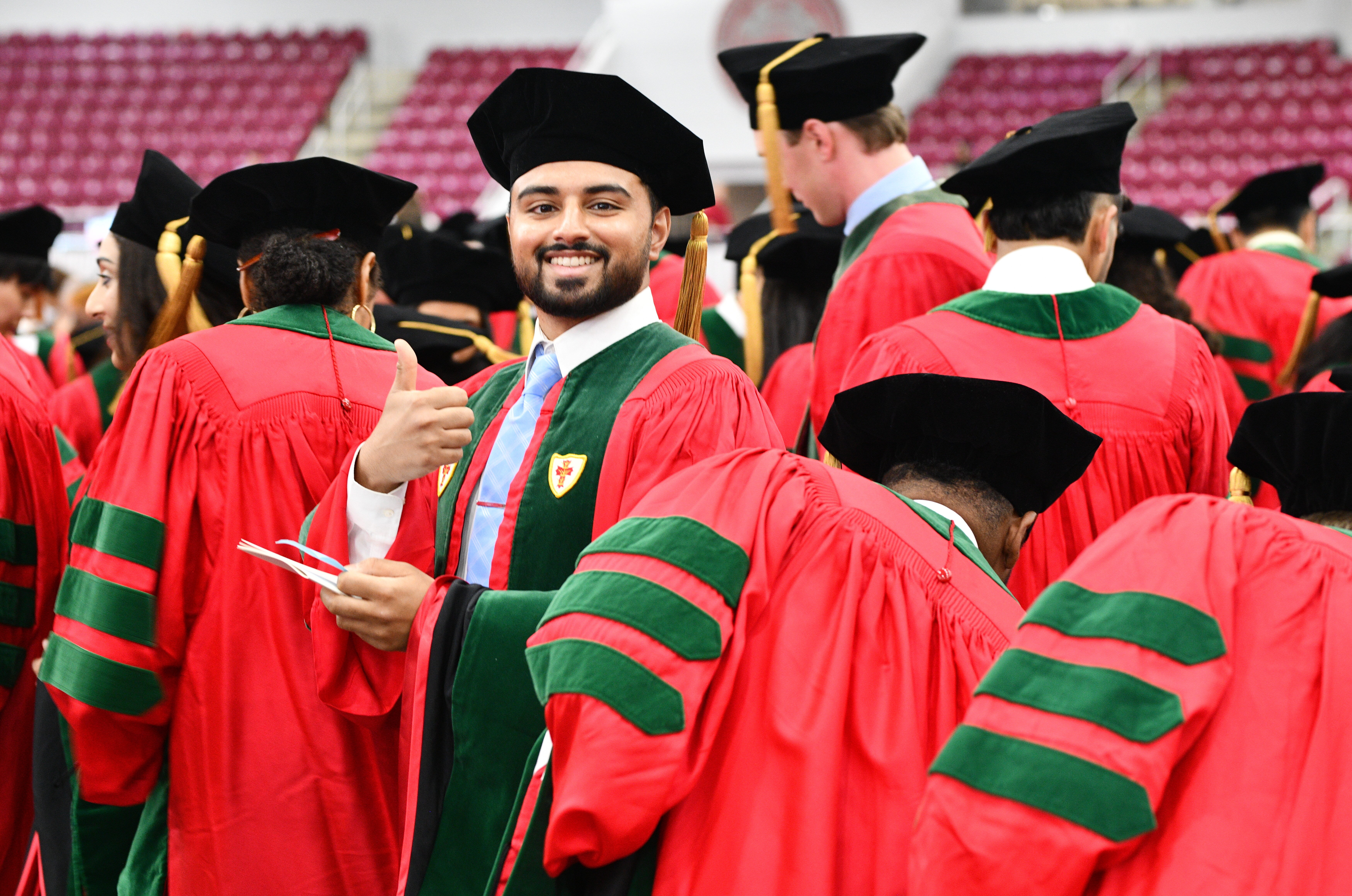 students in regalia walking to their seats, one looks back and gives thumbs up