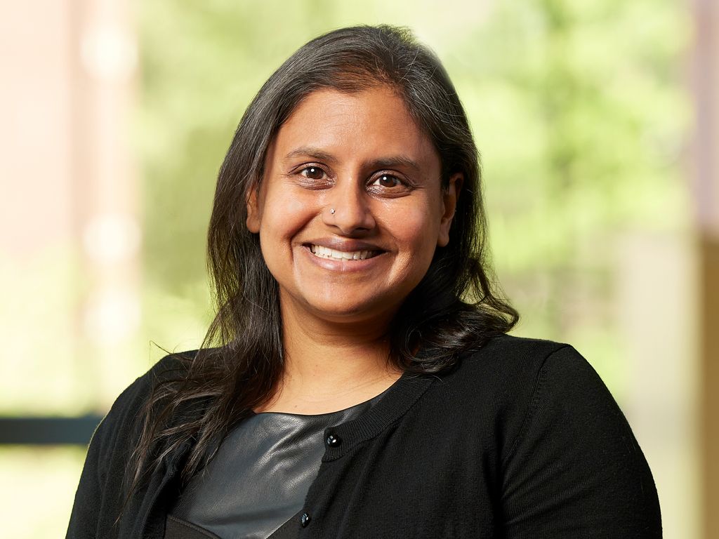 head and shoulders of Padma Kandai wearing dark jacket, long brown hair broad smile