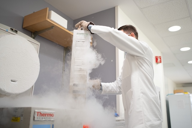 Man in white protective gear and gloves taking sample out of liquid nitrogen