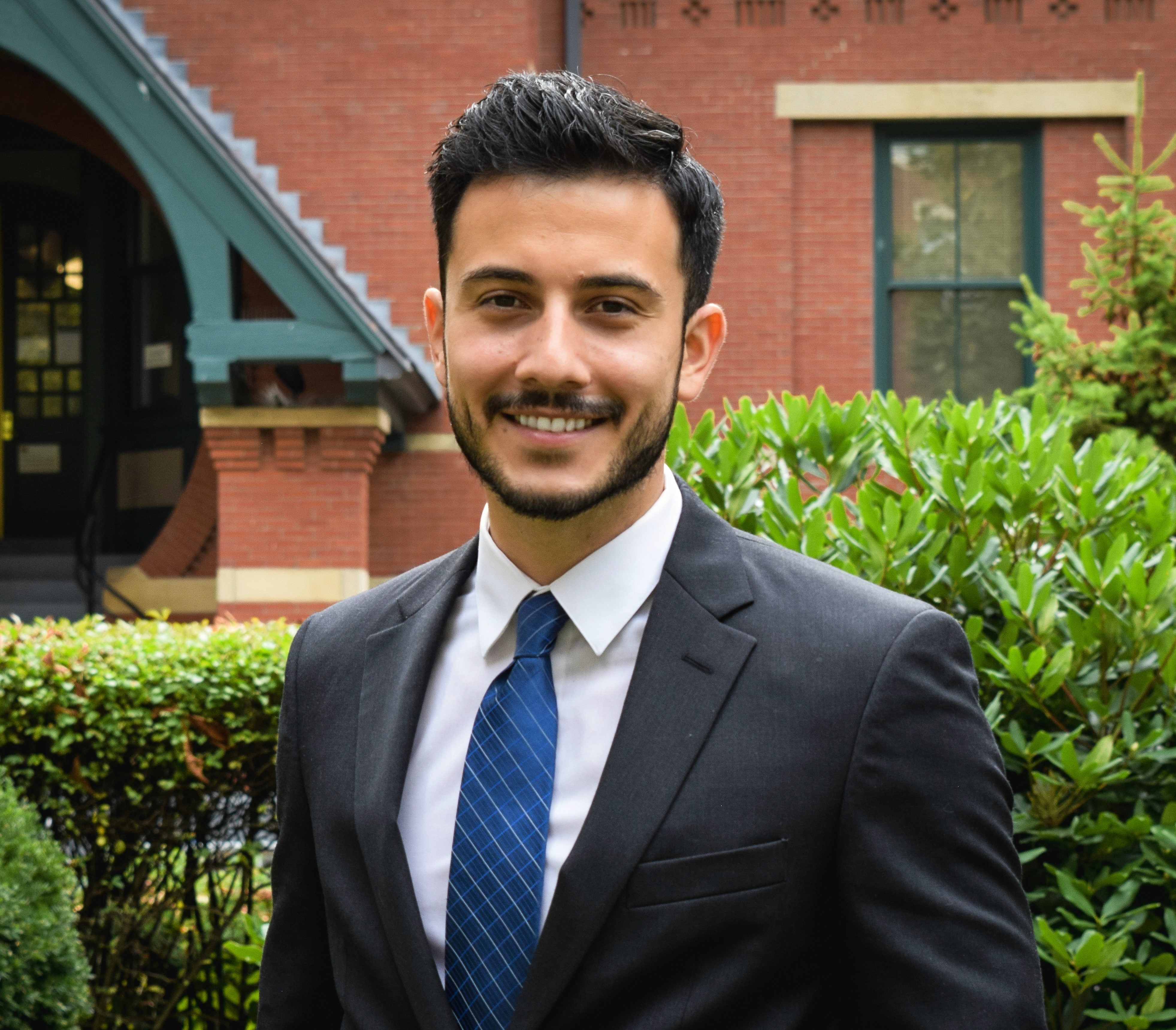 head and shoulders image of Jhonatan Vasquez in dark suit, whtie shirt, blue tie, standing outside