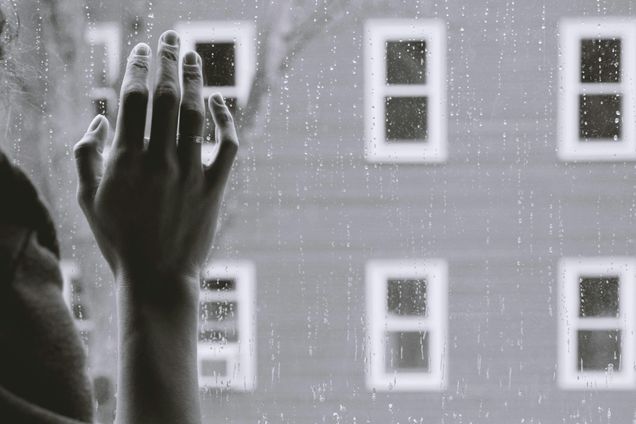 gray tones person standing in shadow in front of window with rain facing brick building