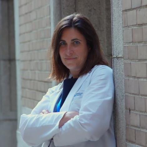Portrait of Alysse Wurcel wearing whitecoat leading again light colored brick wall outside