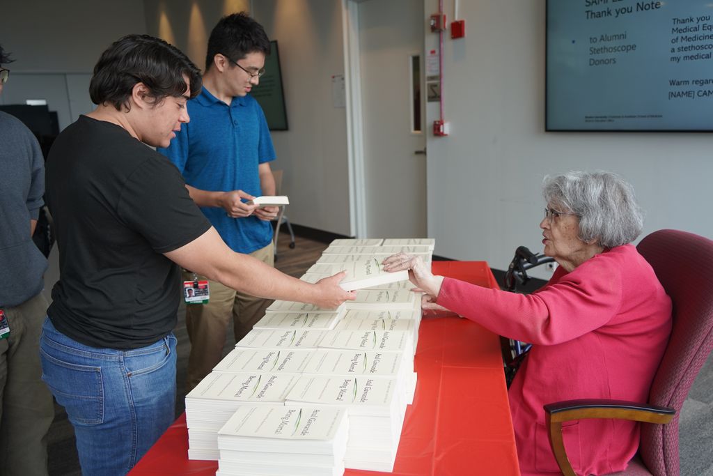 Seated woman handing out copies of a book