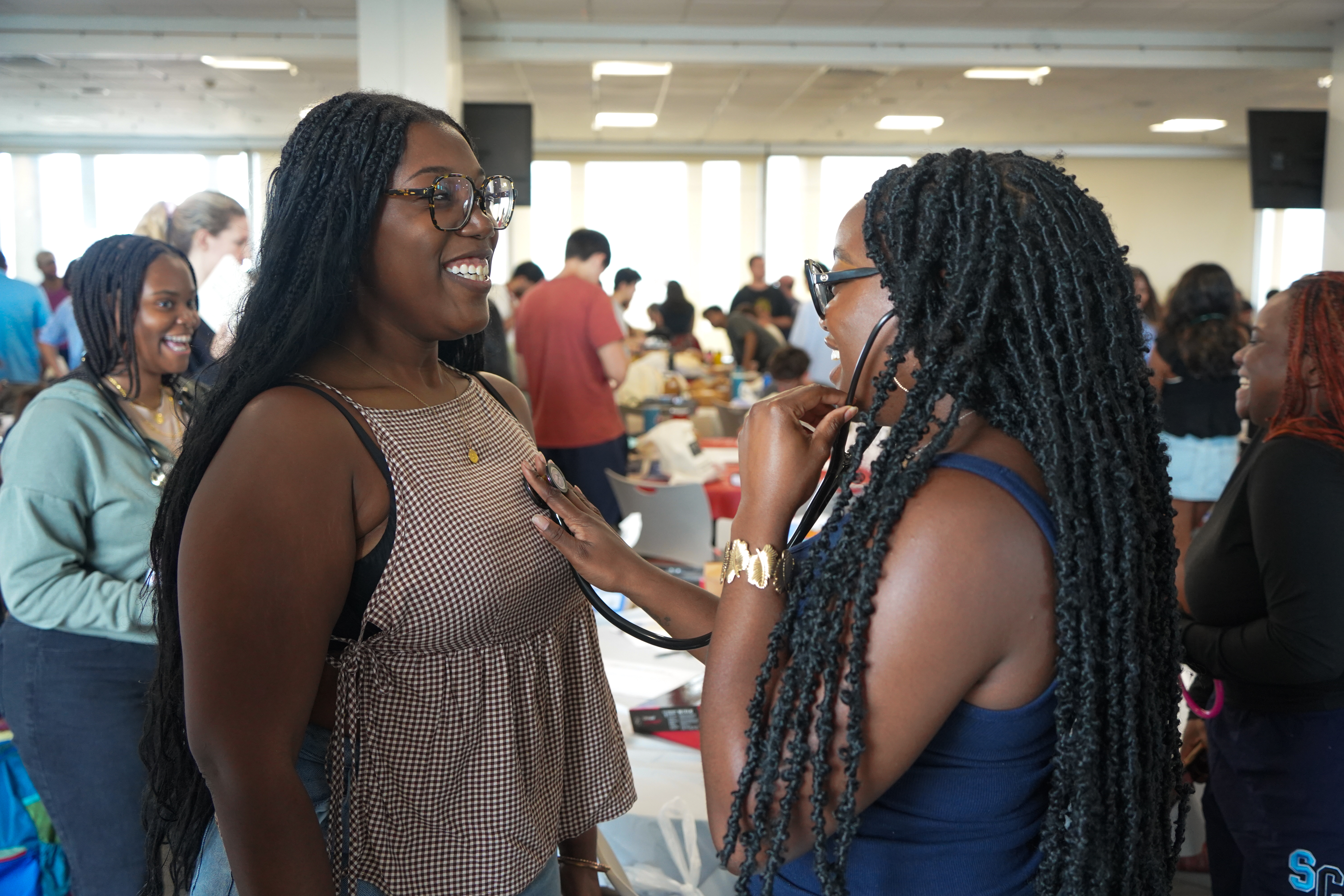 Two women medical students facing each other, one places a stethoscope on the other