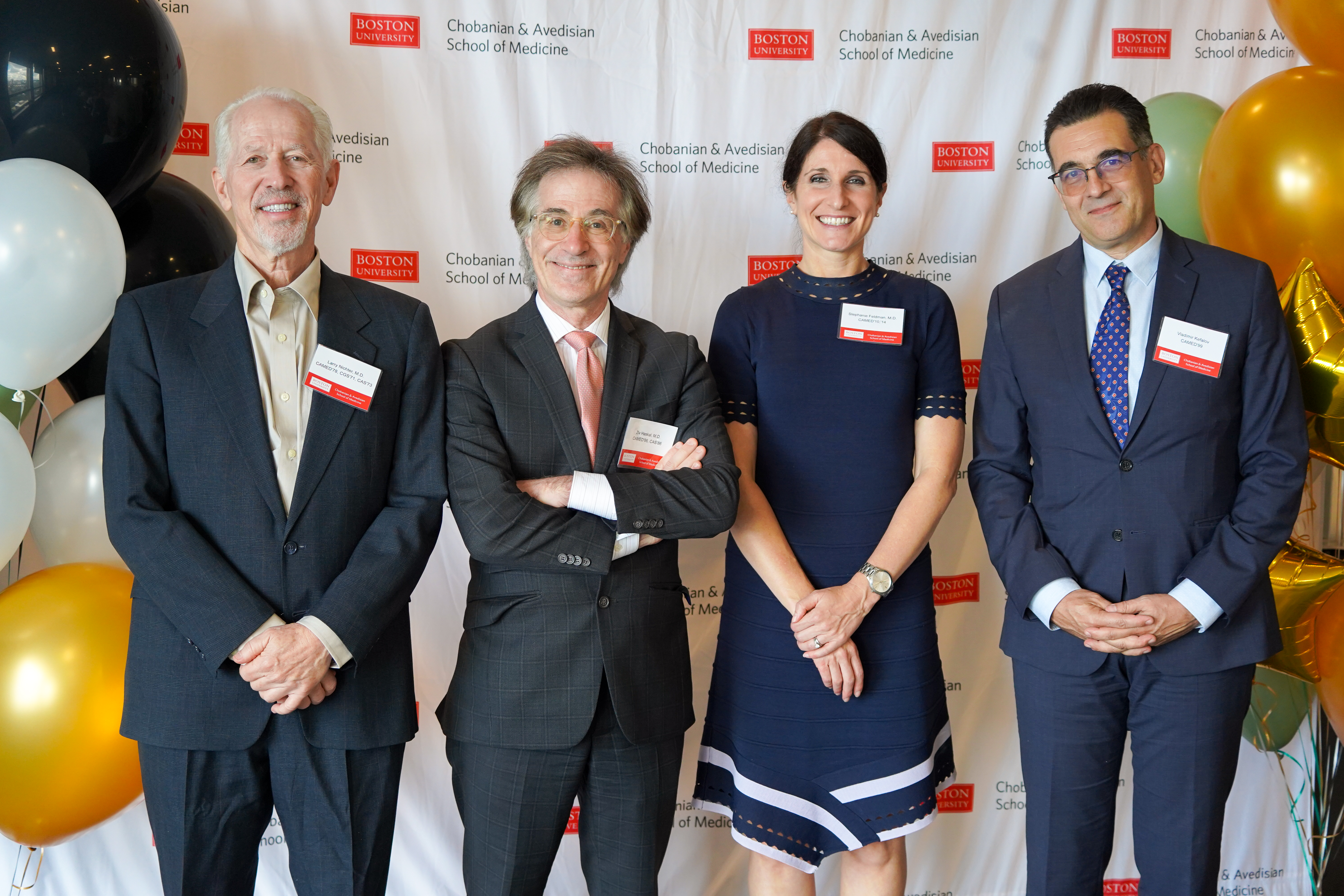 four people lined up infront of SOM banner with white and gold balloons on sides