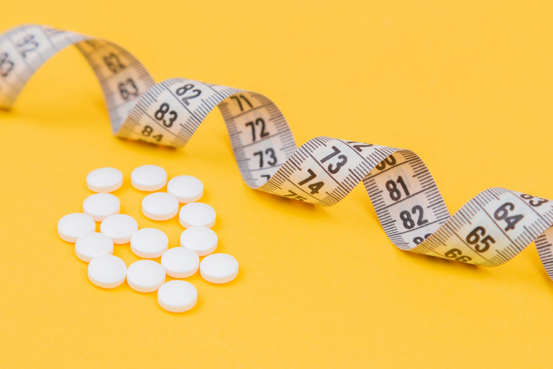 White measuring tape with a white pills, white vitamin on a yellow background.