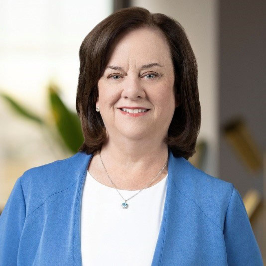 Head and shoulders shot of Cathi Thomas wearing blue jacke and white shirt, brown hair smiling