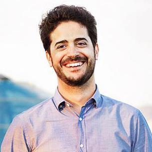 Man with dark hair and beard wearing light blue shirt smiling