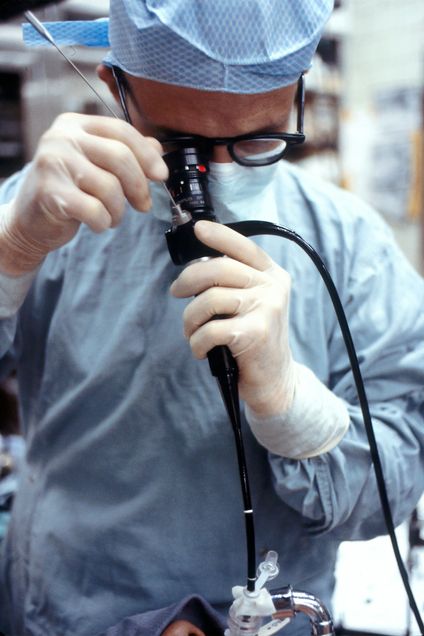 Man in blue scrubs and gloves holding black device