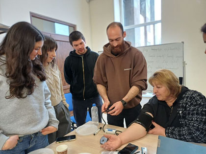 people standing around table, one woman with blood pressure cuff