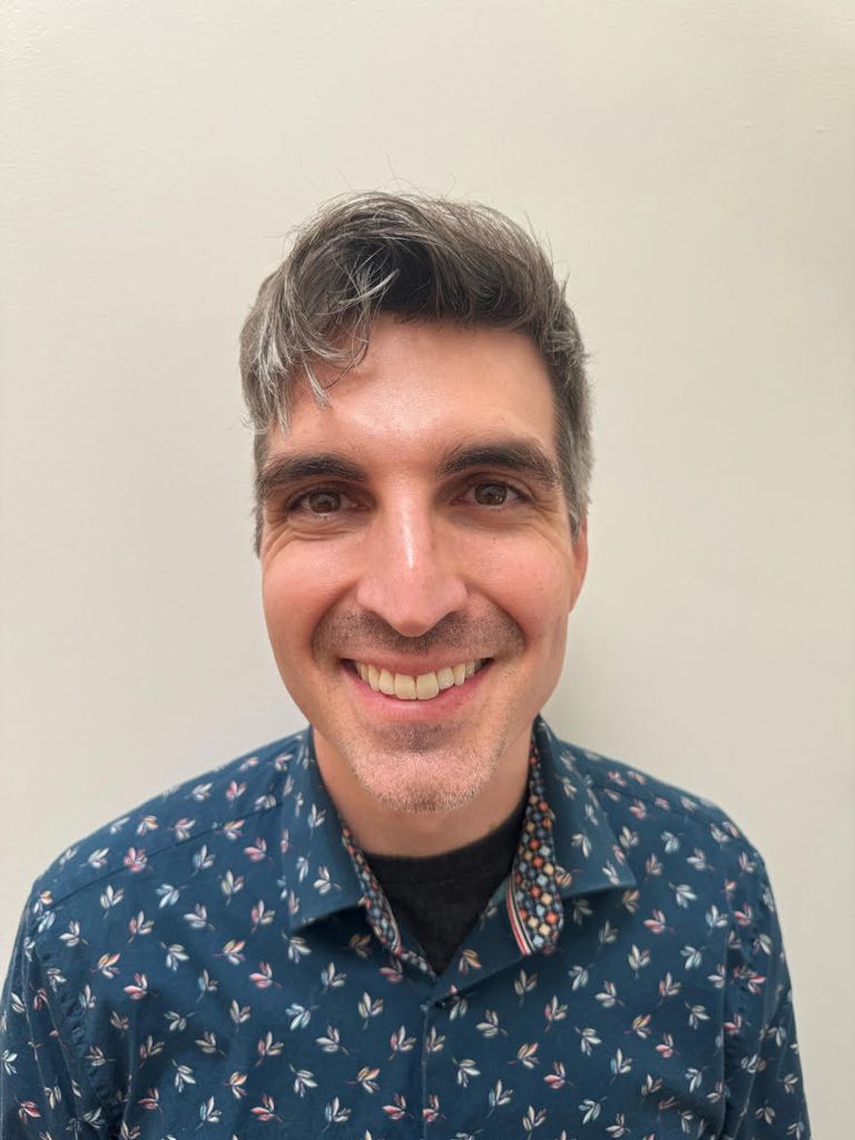 portrait of man wearing blue shirt with pattern smiling broadly