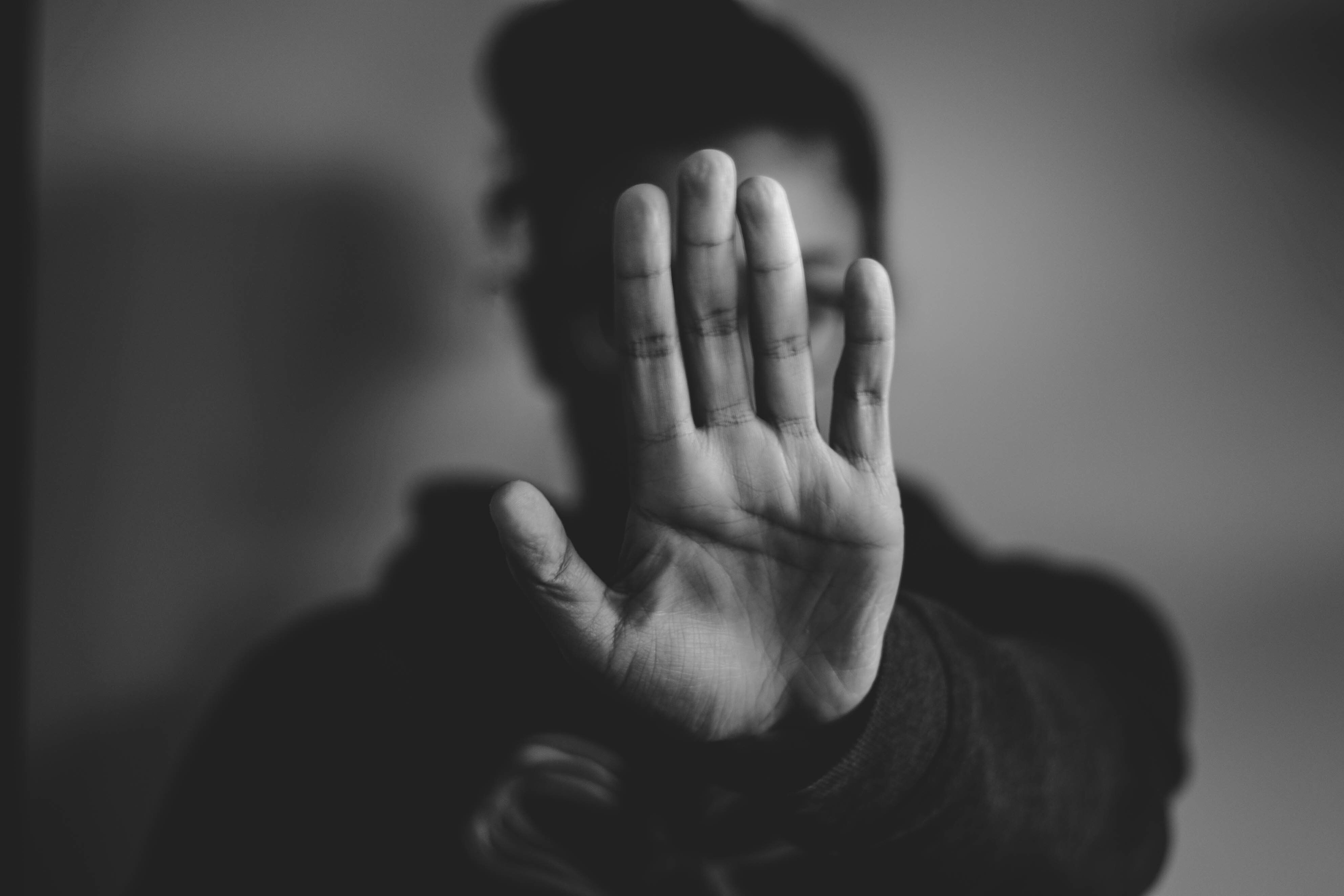 Black and white image of woman holding hand up in front of face to stop someone.