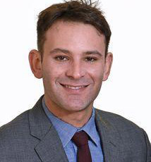 head and shoulders of Jacob Nudel in suit jacket, blue shirt, tie, smiling