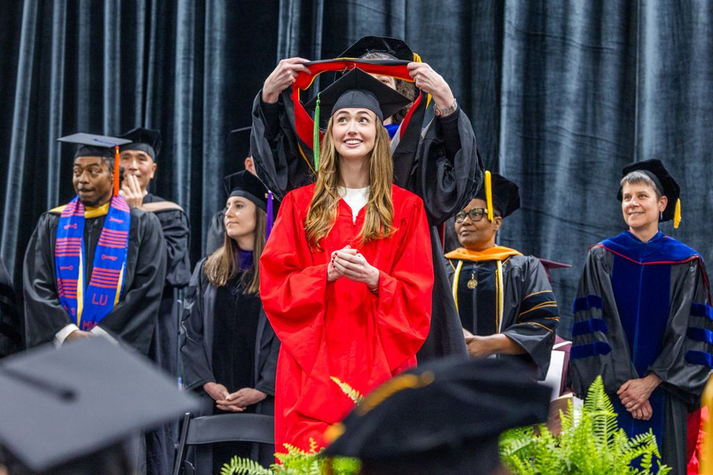 Student on dais with hood over her head smiling broadly