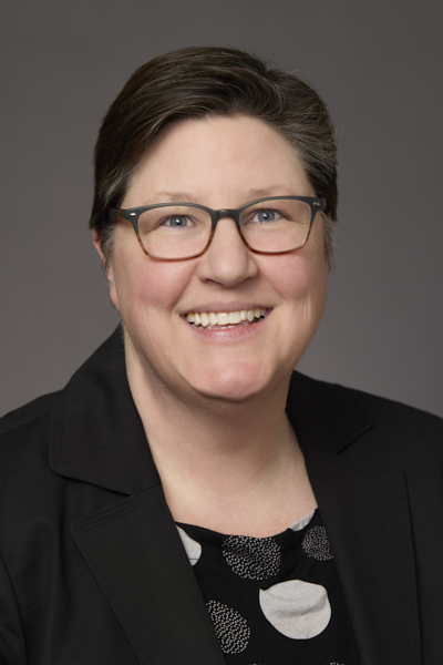Head and shoulders of woman wearing black top, eyeglasses, hair pulled behind her head, smiling